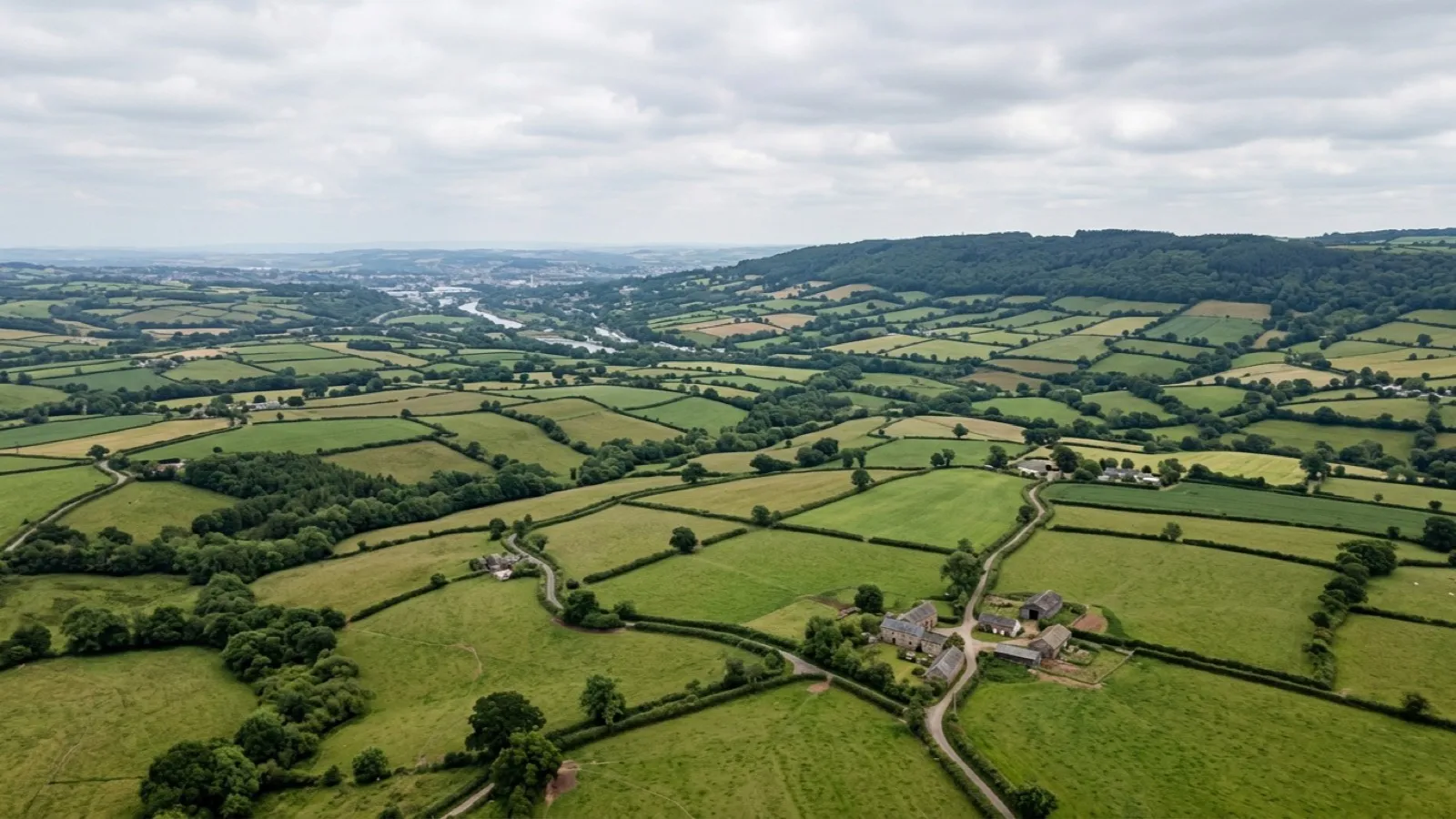 Aerial view across Devon countryside, fields and hedgerows stretching towards a distant ridge under an open sky